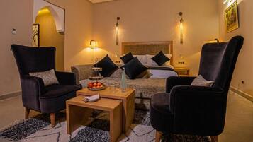 Una habitación de hotel con una cama, dos sillones, una mesita de café y una mesita auxiliar.