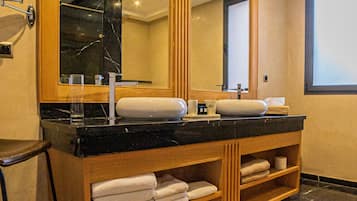 Un baño con tocador de madera, un espejo grande, un espejo redondo, encimera negra y alfombra tejida.