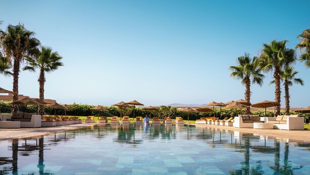 A pool with lounge chairs and umbrellas, surrounded by palm trees and a clear sky. - SUMAHAN SUITES & SPA (Tameslouht)