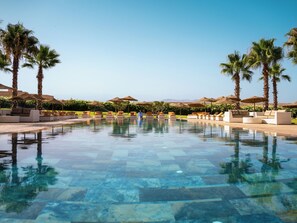 A pool with lounge chairs and umbrellas, surrounded by palm trees and a clear sky. - SUMAHAN SUITES & SPA (Tameslouht)