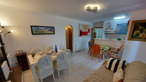 A dining area with a table set for four, a sofa, and a kitchen in the background. - Typical house under the pines with swimming pool and wifi (L'Escala)