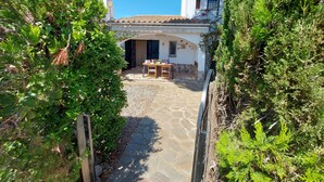 A courtyard with a stone floor, a wooden table and chairs, and a white building with a tiled roof. - Typical house under the pines with swimming pool and wifi (L'Escala)