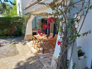 An outdoor dining area with a wooden table and chairs, surrounded by a white wall and greenery. - Typical house under the pines with swimming pool and wifi (L'Escala)