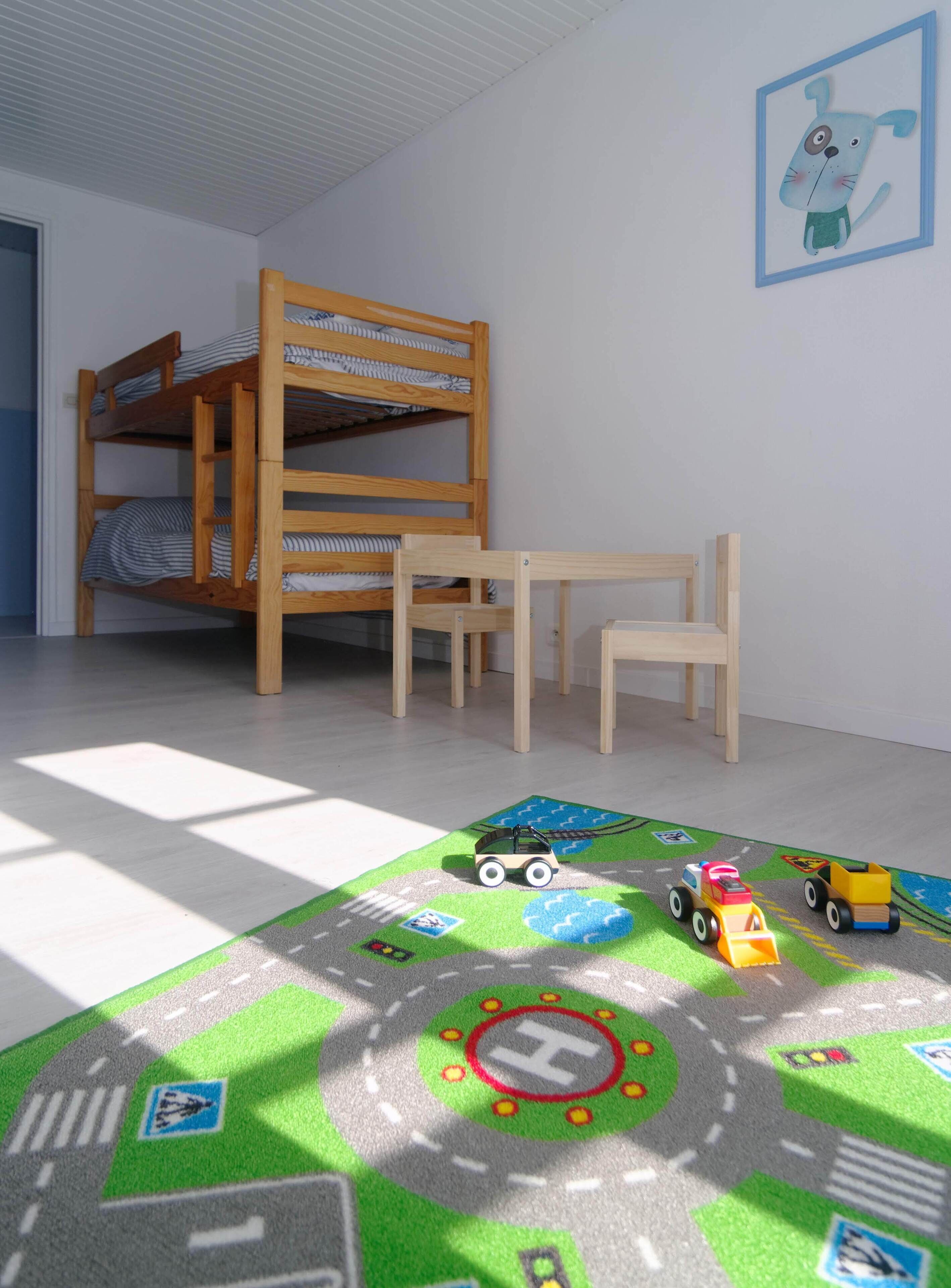 A child's room with bunk beds, a wooden desk, and a play mat with toy vehicles.