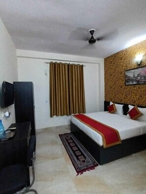 Une chambre d’hôtel équipée d’un lit, d’un bureau, d’une chaise, d’une télévision et d’un ventilateur de plafond.