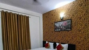 A bedroom with a bed, a patterned wall, a ceiling fan, and a window with curtains. - Hotel CityMax Inn (Greater Noida)