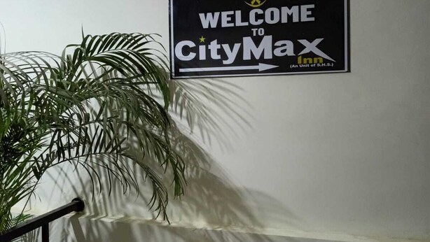 A welcome sign for CityMax Inn, a sign on a white wall, a potted plant, and a staircase. - Hotel CityMax Inn (Greater Noida)