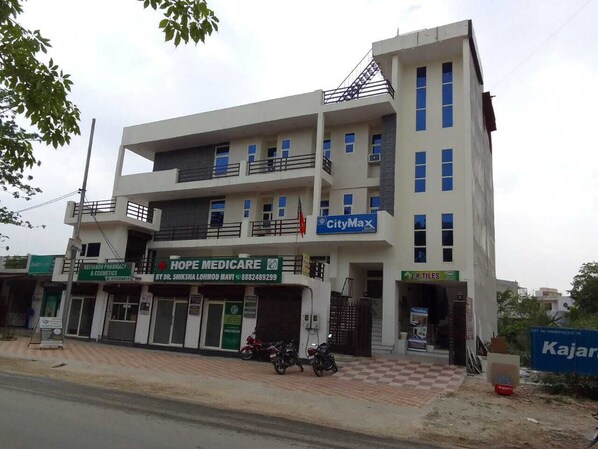 Un immeuble à plusieurs étages abritant divers commerces, notamment une pharmacie, un centre médical et un magasin de carrelage.