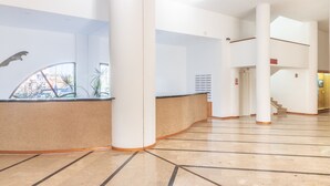 Een ruime lobby met een gebogen receptiebalie, grote kolommen en een trap naar een hoger niveau.