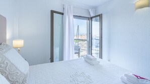 Hotelkamer met een bed, nachtkastje, lamp, raam met gordijnen en uitzicht op de stad.