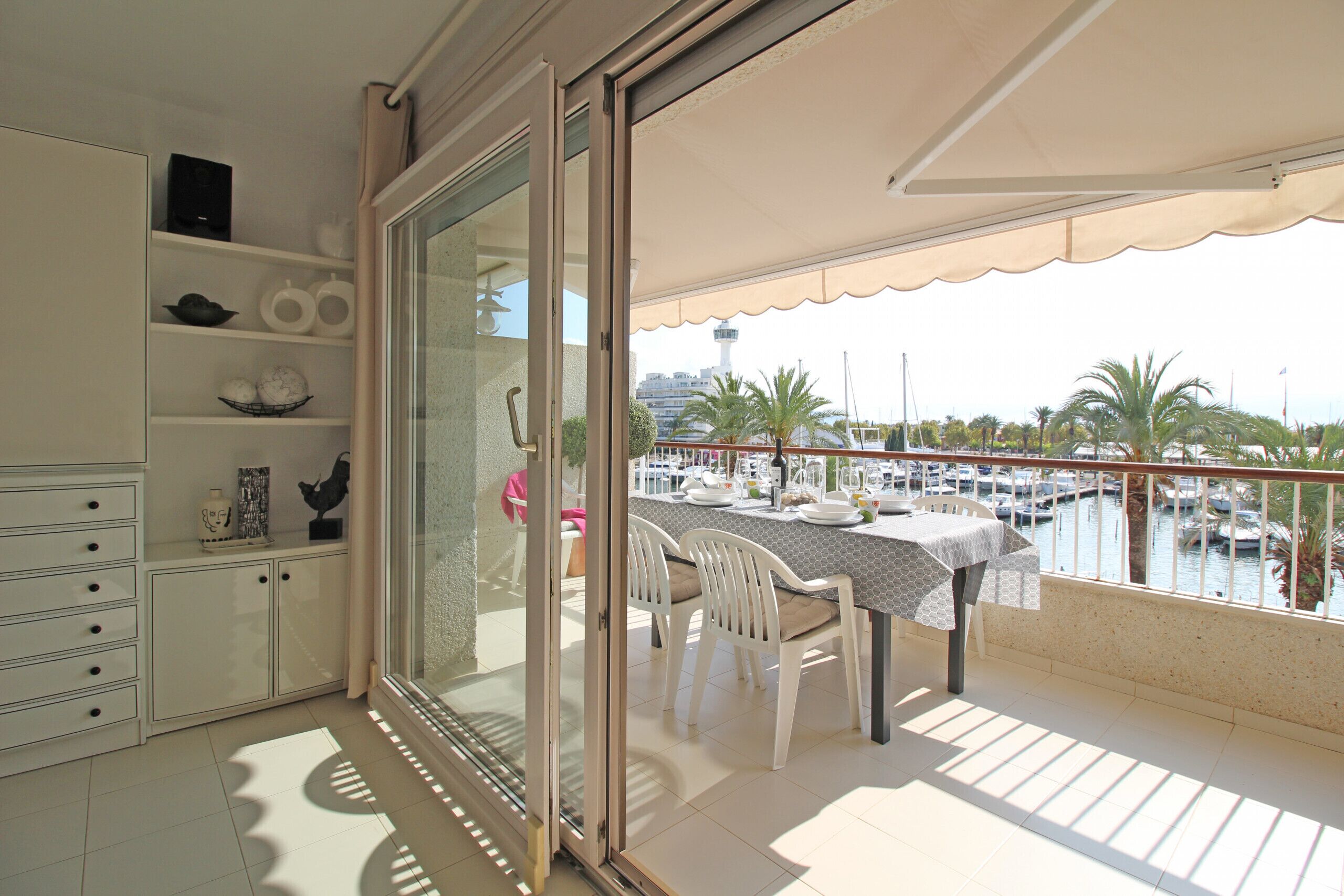 A balcony with a table and chairs, a view of a marina, and a cityscape in the background.