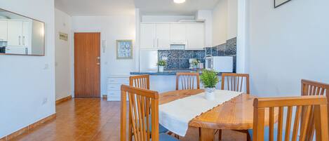Een moderne keuken met witte kastjes, een betegelde spatwand en een houten eettafel met blauwe stoelen.