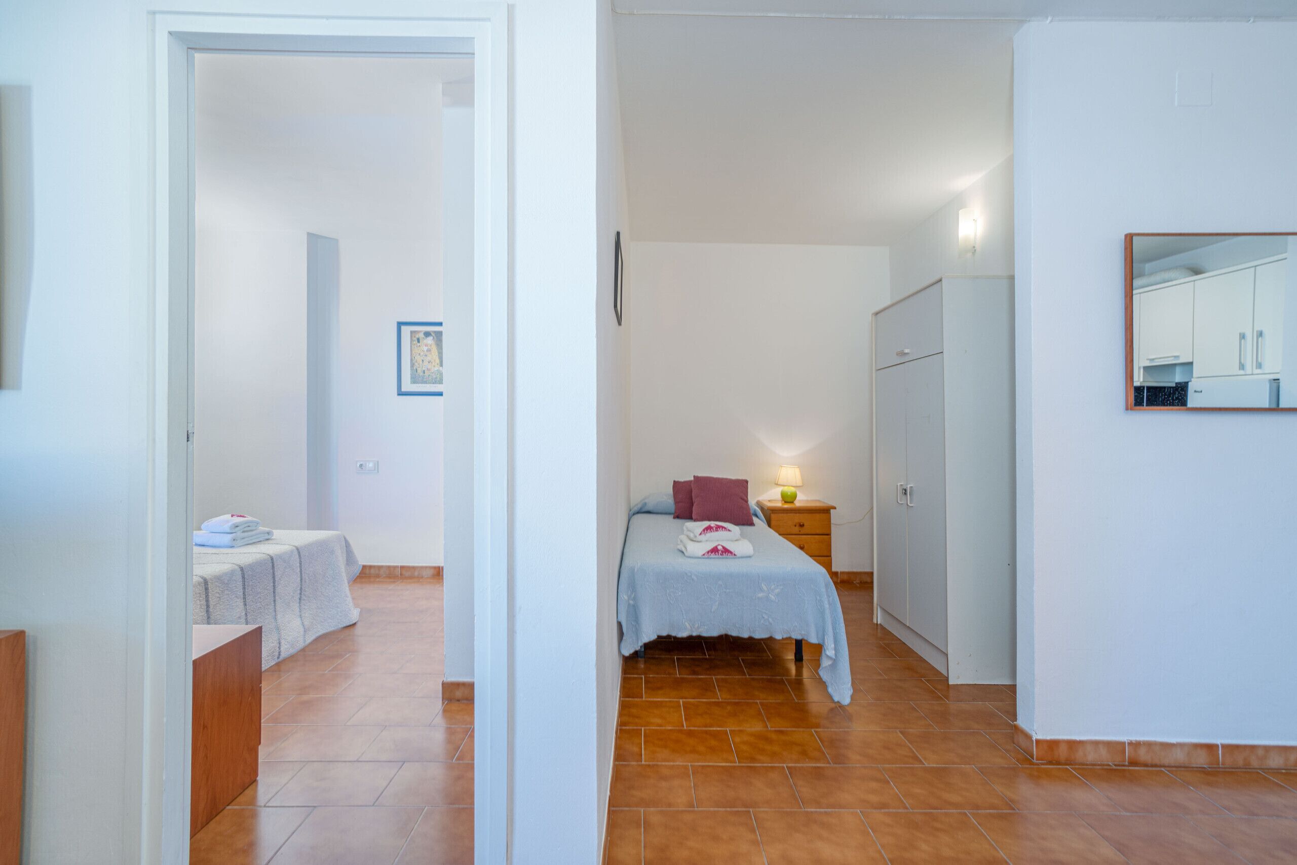 Quarto com cama, mesa de cabeceira, guarda-roupa e banheiro visível por uma porta aberta.