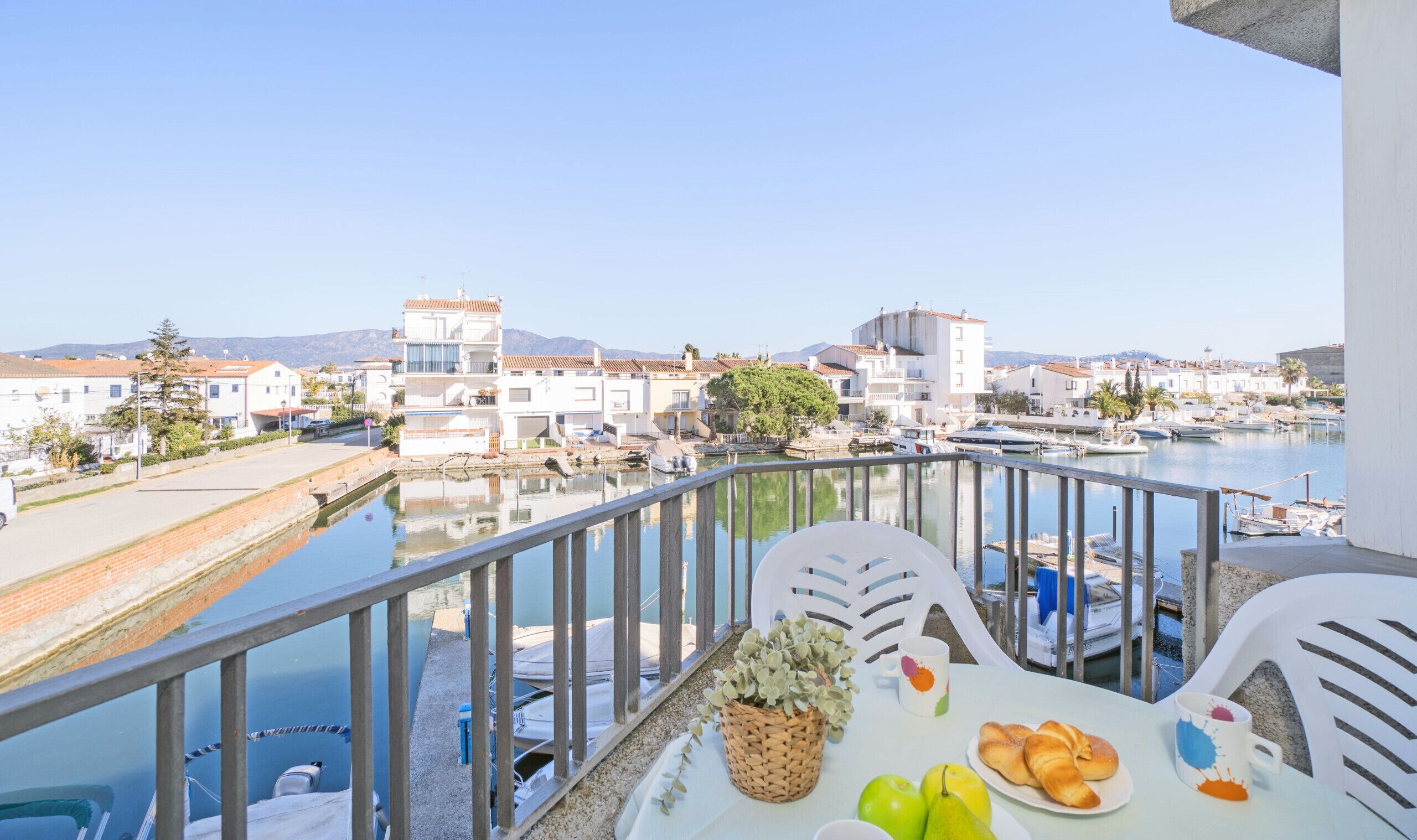 A balcony with a table set for breakfast, overlooking a marina with boats and buildings.