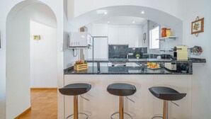 Une cuisine moderne dotée d’un plan de travail en marbre, de trois tabourets de bar et donnant sur l’espace repas.