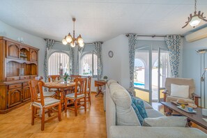 Ampla sala de estar com mesa de jantar, cadeiras, sofá e vista para a piscina.