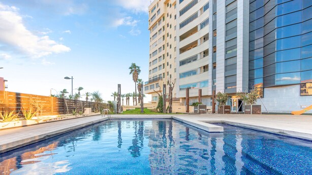 A modern hotel with a swimming pool, a multi-story building, and palm trees.