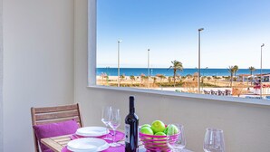 A balcony table with a view of the beach, a bottle of wine, and a basket of apples.