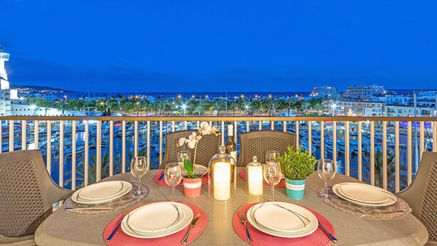 Un área de comedor con una mesa dispuesta para dos, con vista a una marina con barcos y edificios.