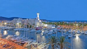 Una marina con numerosos barcos amarrados, un faro destacado y un fondo de edificios y colinas.