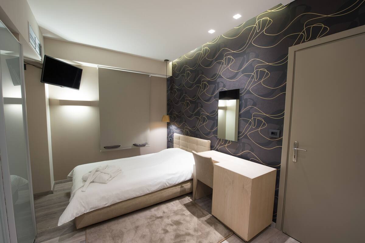 Quarto moderno com cama, escrivaninha, espelho e televisão.