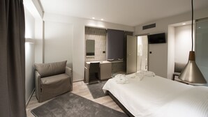 Una camera d'albergo moderna con un letto, una scrivania, una sedia, un angolo trucco e una TV.