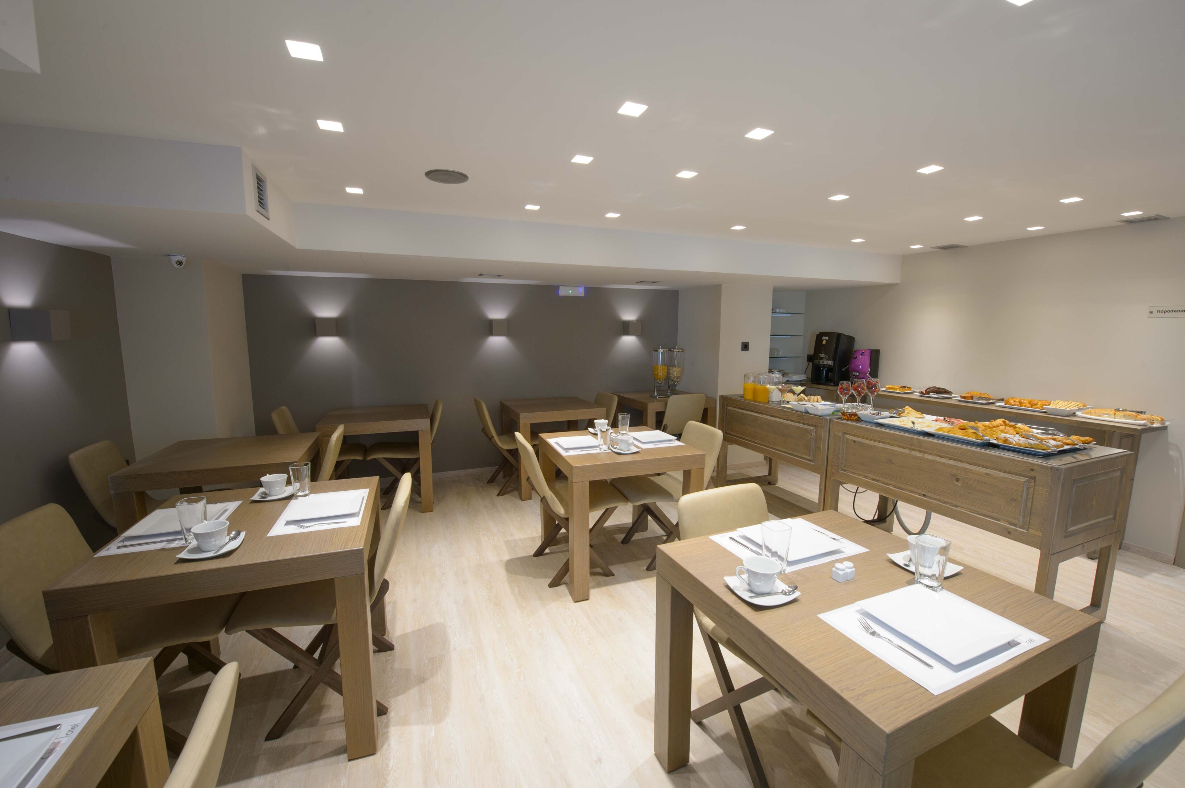 Un comedor moderno con mesas y sillas de madera, un bufé con diferentes opciones de comida y una máquina de café.