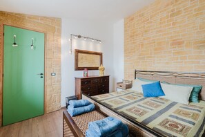 Quarto com porta verde, cama com roupa de cama estampada, cômoda e espelho com iluminação.