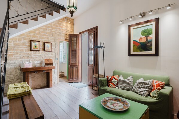 A living room with a staircase, a green sofa, a wooden bench, a dining table, and a painting on the wall. - Holiday Home 'Roberta' with Sea View, Terrace, Air Conditioning & Wi-Fi (Torretta Granitola)