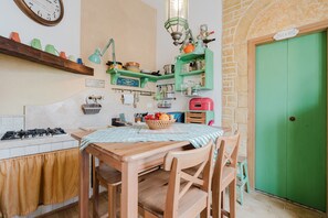 Cozinha com fogão a gás, mesa de madeira, cadeiras e uma porta verde.