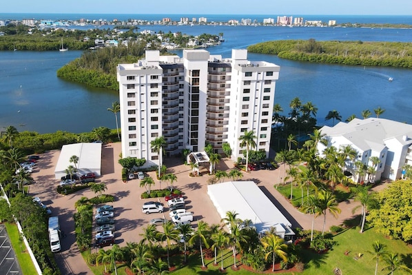 A high-rise hotel with multiple floors, a parking lot, and a view of the surrounding water and greenery.