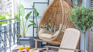 Een balkon met een rieten stoel, een eettafel met fruit en een boek, en potplanten.