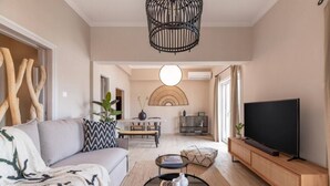 Een moderne woonkamer met een bank, salontafel, televisie en een eethoek op de achtergrond.