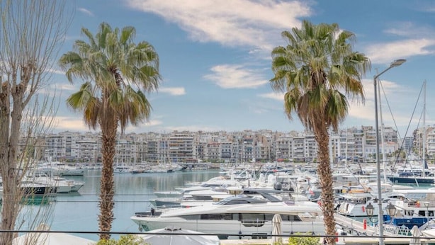 Een jachthaven met talloze jachten afgemeerd, palmbomen en een stadsgezicht op de achtergrond.