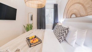 Een moderne hotelkamer met een bed, een televisie, een rieten hoofdbord en een schaal fruit op het nachtkastje.