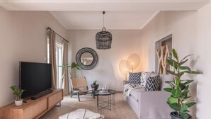 Een moderne woonkamer met een flatscreen televisie, een houten kast, een ronde spiegel, een bank met opvallende kussens, een salontafel en een hanglamp.