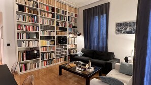 A living room with a large bookshelf, a black sofa, a coffee table, and a blue curtain. - Beautiful apartment within walking distance of St. Peter's (Roma)