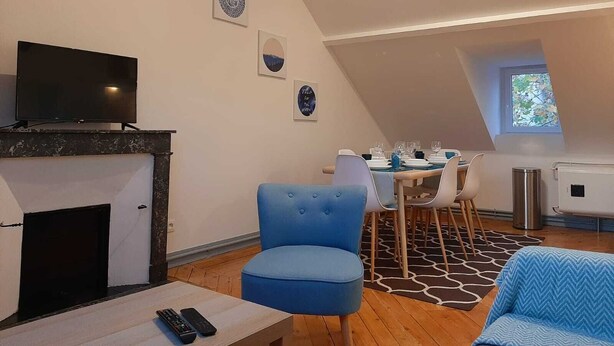 En hyggelig stue med pejs, et fjernsyn og et spiseområde med et bord dækket til fire personer.