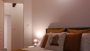 En pænt redt seng med et brunt tæppe, en sengetavlelampe og en vægmonteret lampe.