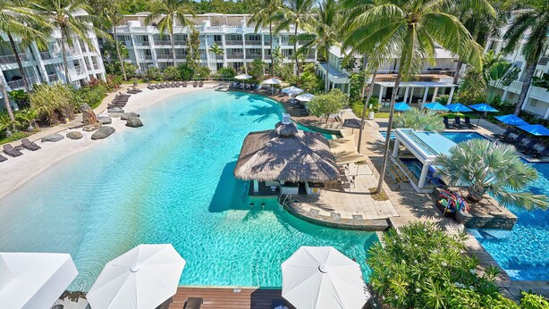 A resort with a large pool, palm trees, and a thatched-roof structure.