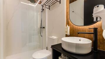 Un baño moderno con ducha envuelta en vidrio, un inodoro blanco y un lavamanos negro con un espejo grande.