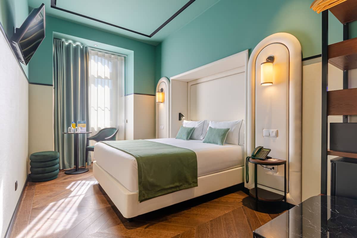 Ein modernes Hotelzimmer mit einem großen Bett, einem Schreibtisch, einem Stuhl und einem kleinen Tisch mit Telefon.