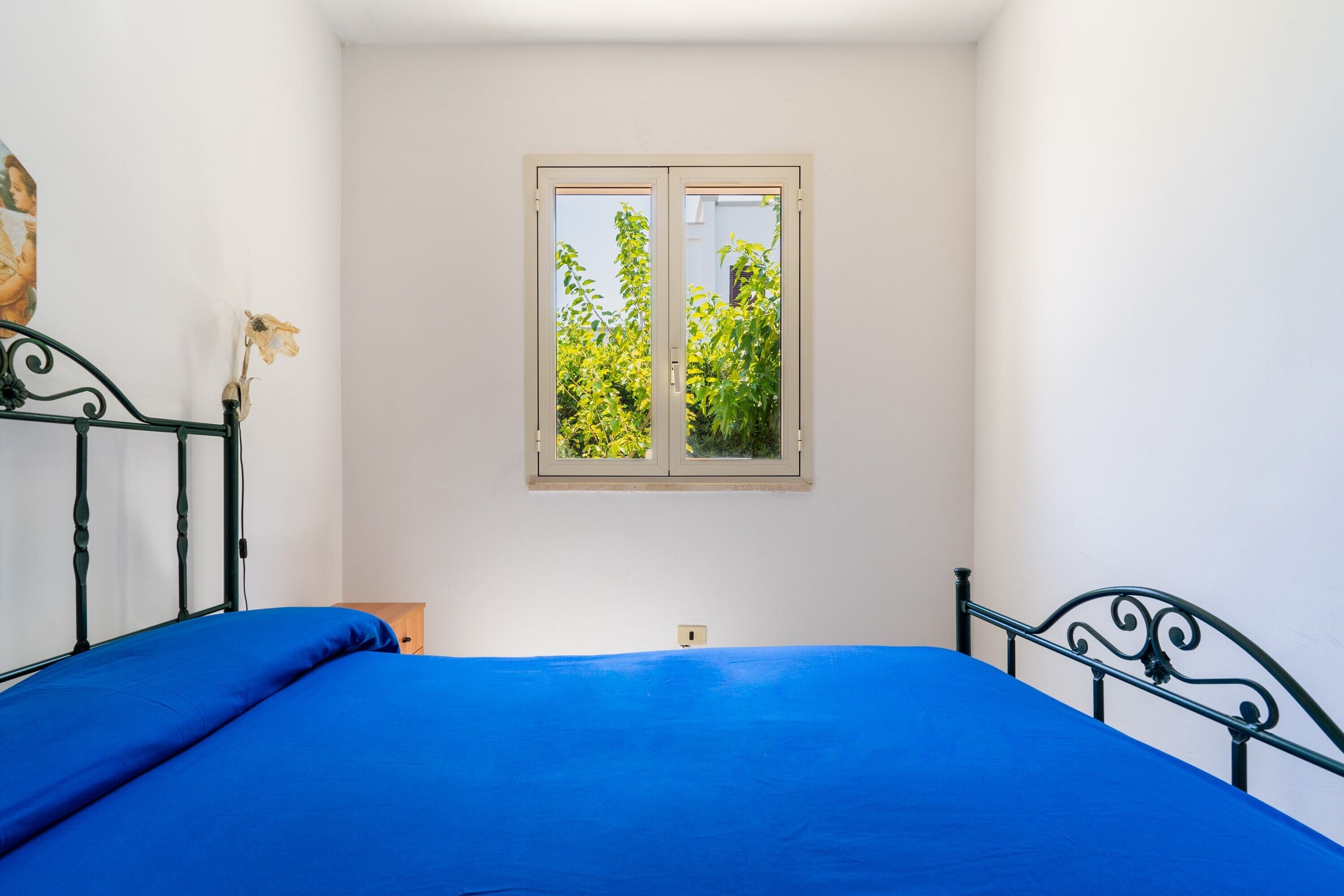 Une chambre à coucher avec un lit, une fenêtre donnant sur un espace verdoyant et un luminaire fixé au mur.