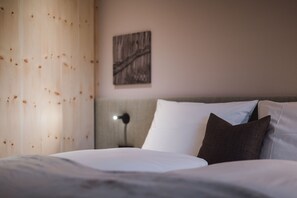 Un lit bien fait, avec des oreillers blancs et foncés, une tête de lit en bois et une œuvre d’art accrochée au mur.