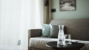Un salon avec un canapé, une petite table ronde, une bouteille d’eau et un verre posés sur la table.