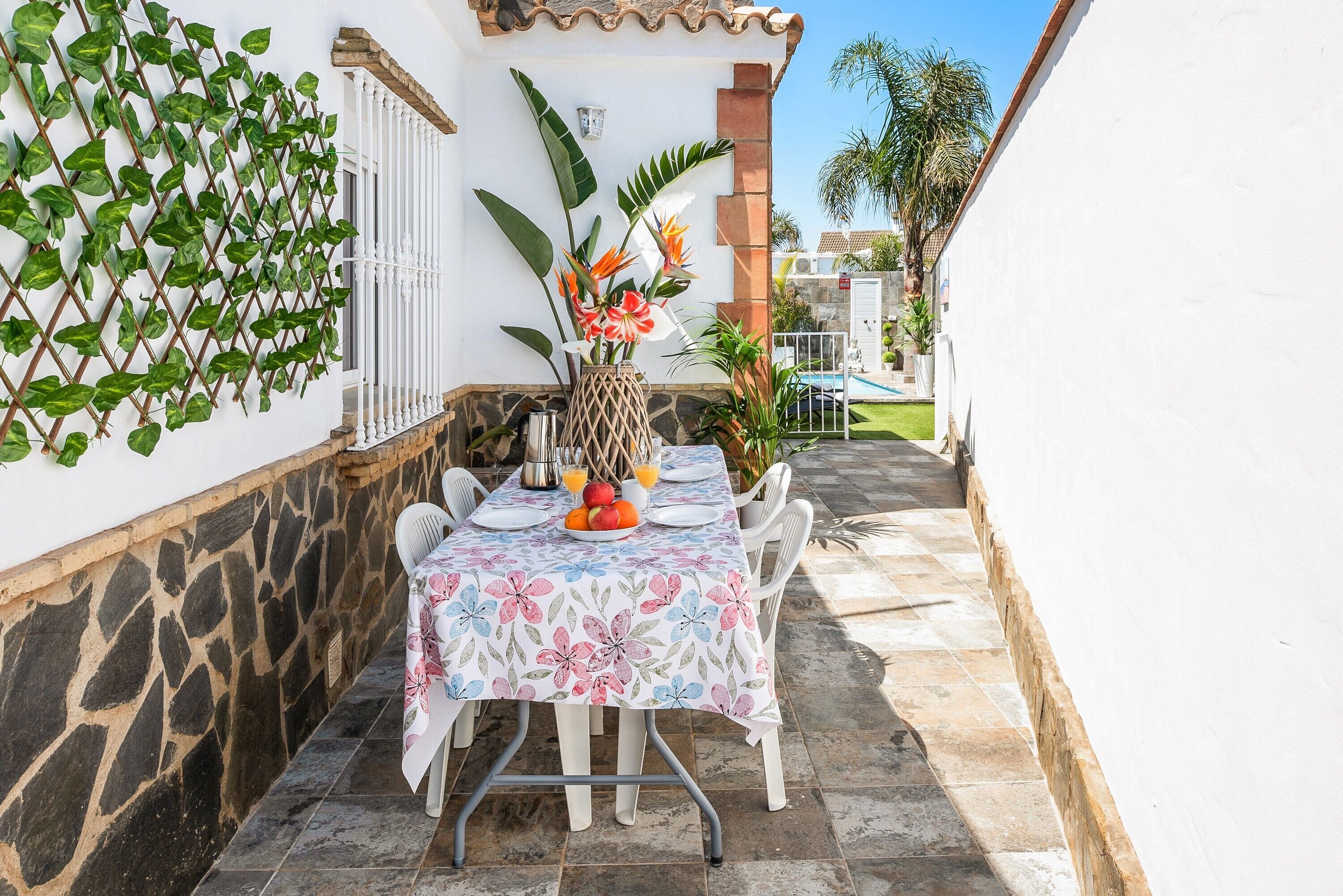 Una mesa de comedor con mantel floral, sillas blancas y un jarrón con flores.