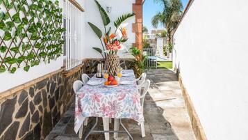 Una mesa de comedor con mantel floral, sillas blancas y un jarrón con flores.
