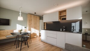 A modern kitchen with white cabinets, a black countertop, and a built-in oven. There is a dining area with a wooden table and chairs. - Apartment 'Nature Berg' with Mountain View, Terrace & Wi-Fi (Luttach)