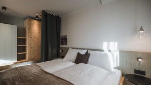 A hotel room with a bed, a wooden wardrobe, a small table, and a wall-mounted light fixture. - Apartment 'Nature Berg' with Mountain View, Terrace & Wi-Fi (Luttach)