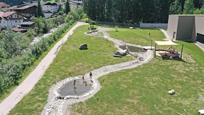 Un parque con un arroyo serpenteante, zonas de picnic y un parque infantil.